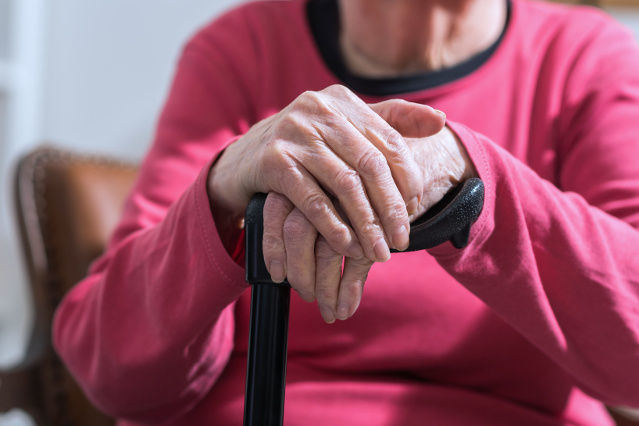 die Hände einer sitzende ältere Frau fassen einen Gehstock (verweist auf: Gesetzliche Rentenversicherung)