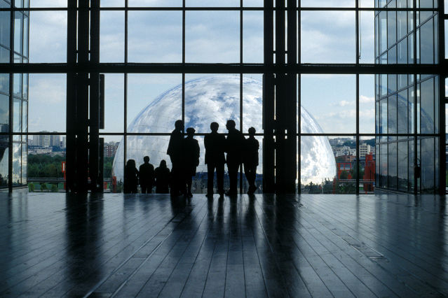 Personen stehen in einem Raum vor einer großen Glasfront 