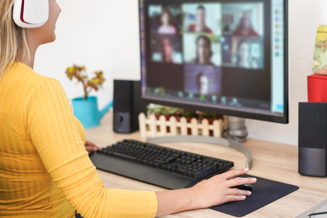 eine Frau mit Kopfhörer sitzt vor einem Laptopbildschirm auf dem viele Kacheln mit Personen abgebildet sind (verweist auf: Nutzung von Videokonferenzdiensten)